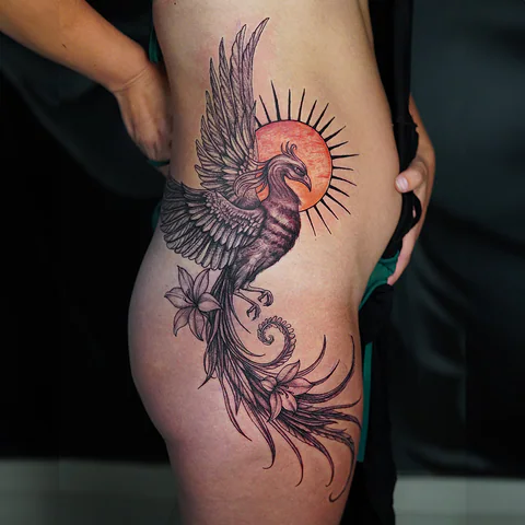 Phoenix thigh tattoo with red sun and floral design